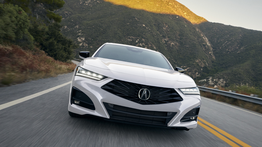 Gros plan avant d’une TLX blanche roulant en direction de la caméra sur une autoroute en montagne.