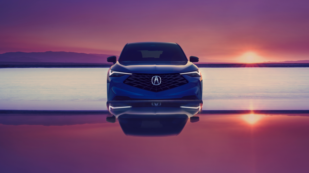 Front view of a blue Acura ADX with a sunset in the background.