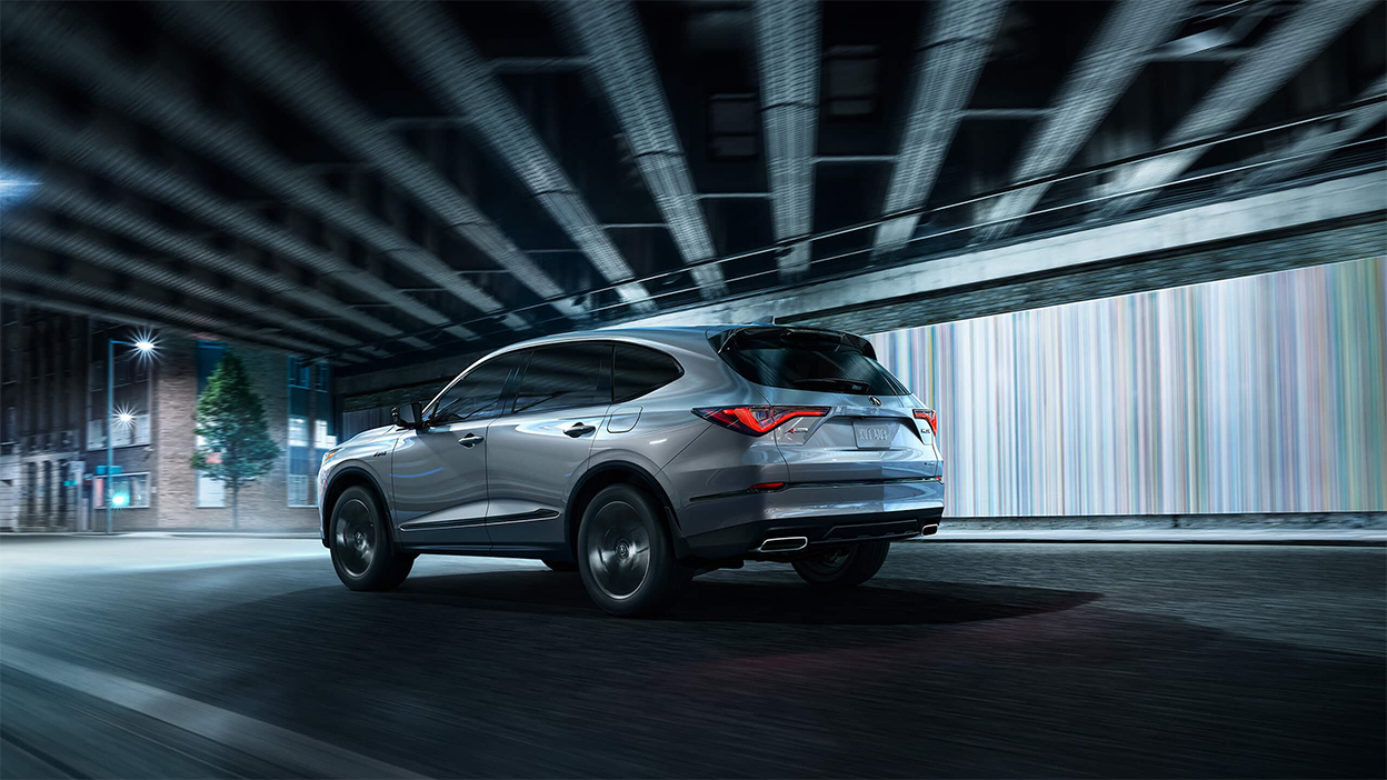 Un MDX gris circulant sous un viaduc en ville.