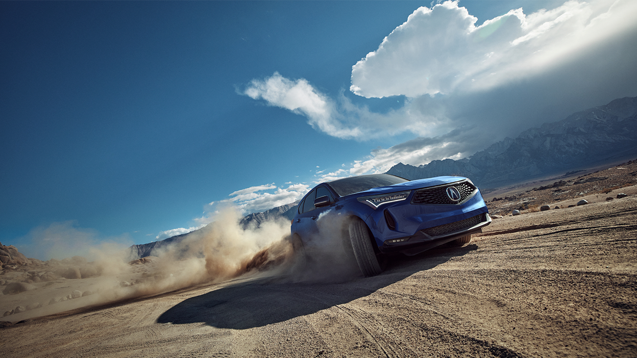 3/4 front view of blue RDX driving on dirt road.