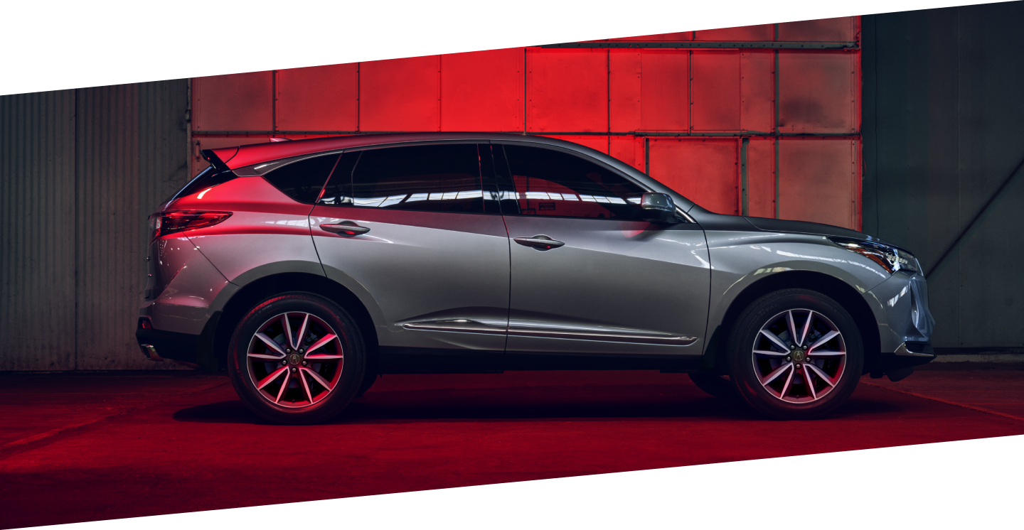 Side view of grey RDX in a warehouse showered in red light in front of a riveted and corrugated metal wall.