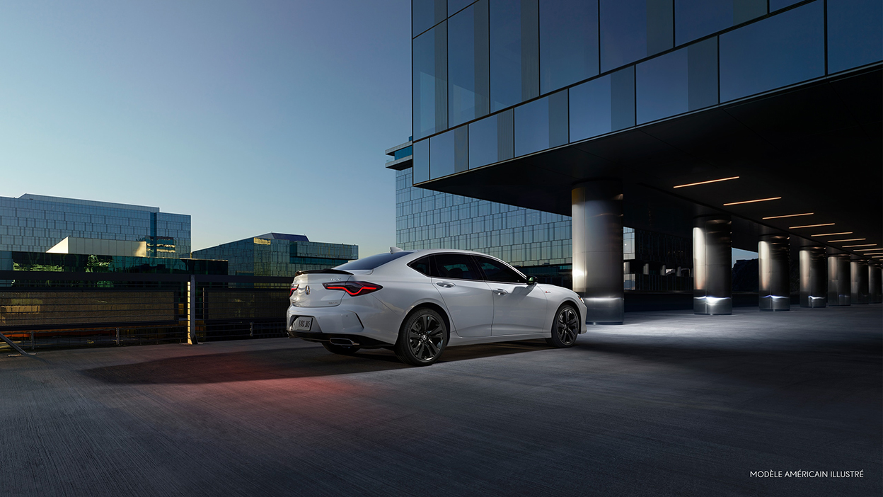 TLX blanche stationnée devant un immeuble de bureaux la nuit.