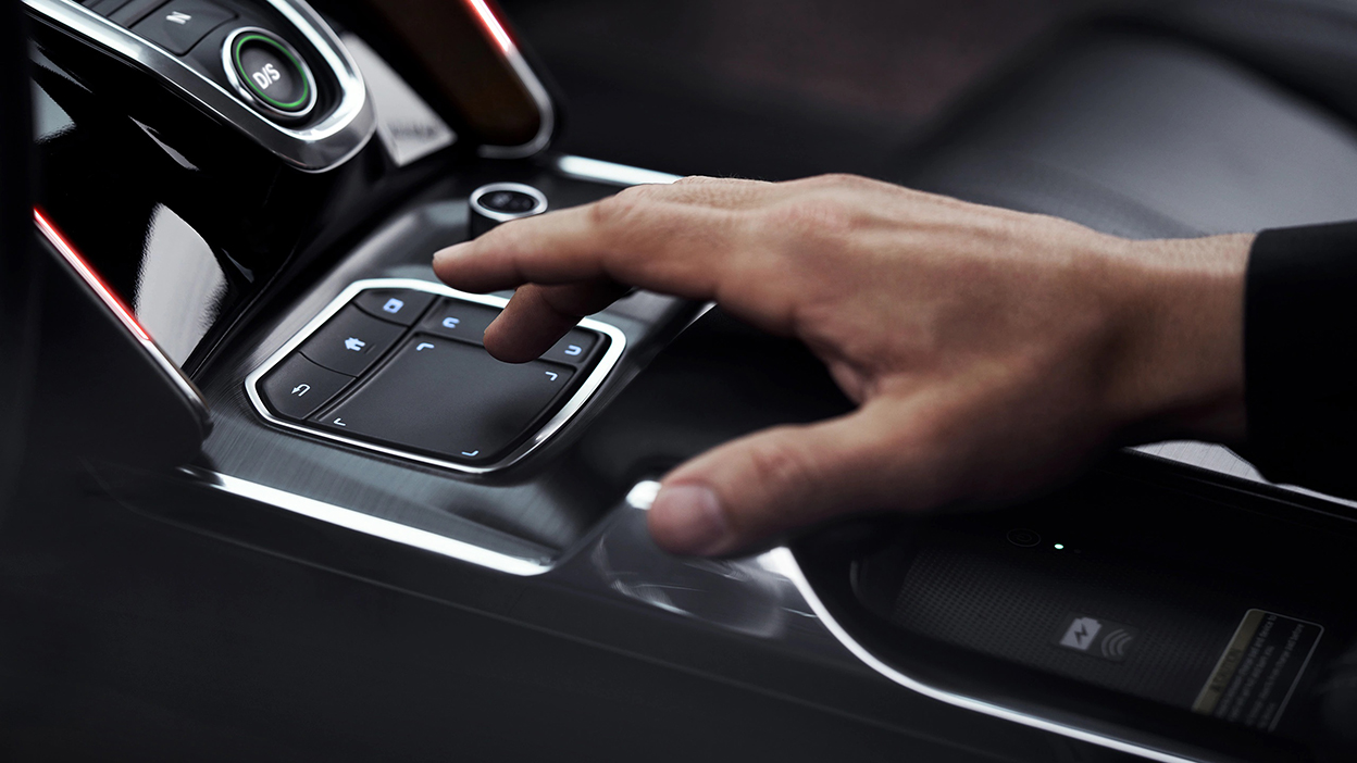 Une main survole l’interface True Touchpad entre les deux sièges avant.