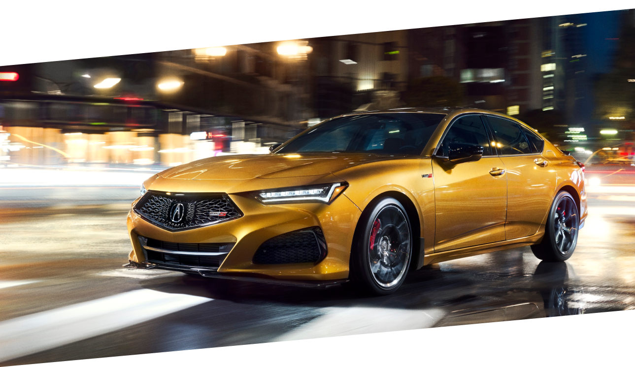 A gold TLX Type S driving on a city street at night. / TLX Type S de couleur or circulant sur une rue urbaine la nuit.