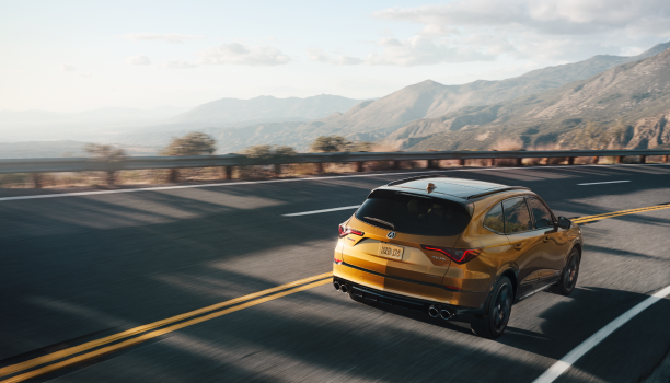 3/4 rear wide view of MDX Type S taking a turn on a mountainous highway in late afternoon sunlight.